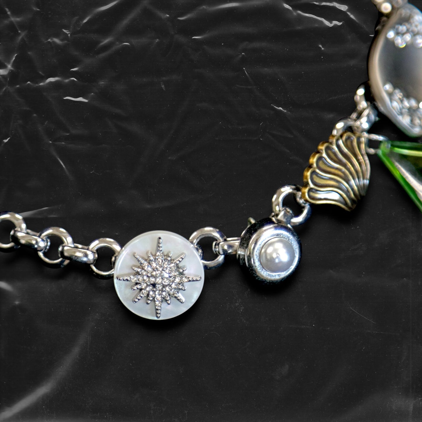 Chockychoker "Witch's Pocket" choker features a whimsical mix of charms, including sculpted silver-toned metal, a delicate milky-white button set with a snowflake-shaped faux crystal, a gold shell charm, faux pearls, a translucent green gemstone pendant, engraved medallions, and abstract vintage elements. The overall style blends eccentricity, fairycore, vintage, witchy, and Y2K aesthetics—perfect for those who embrace unique and expressive fashion.