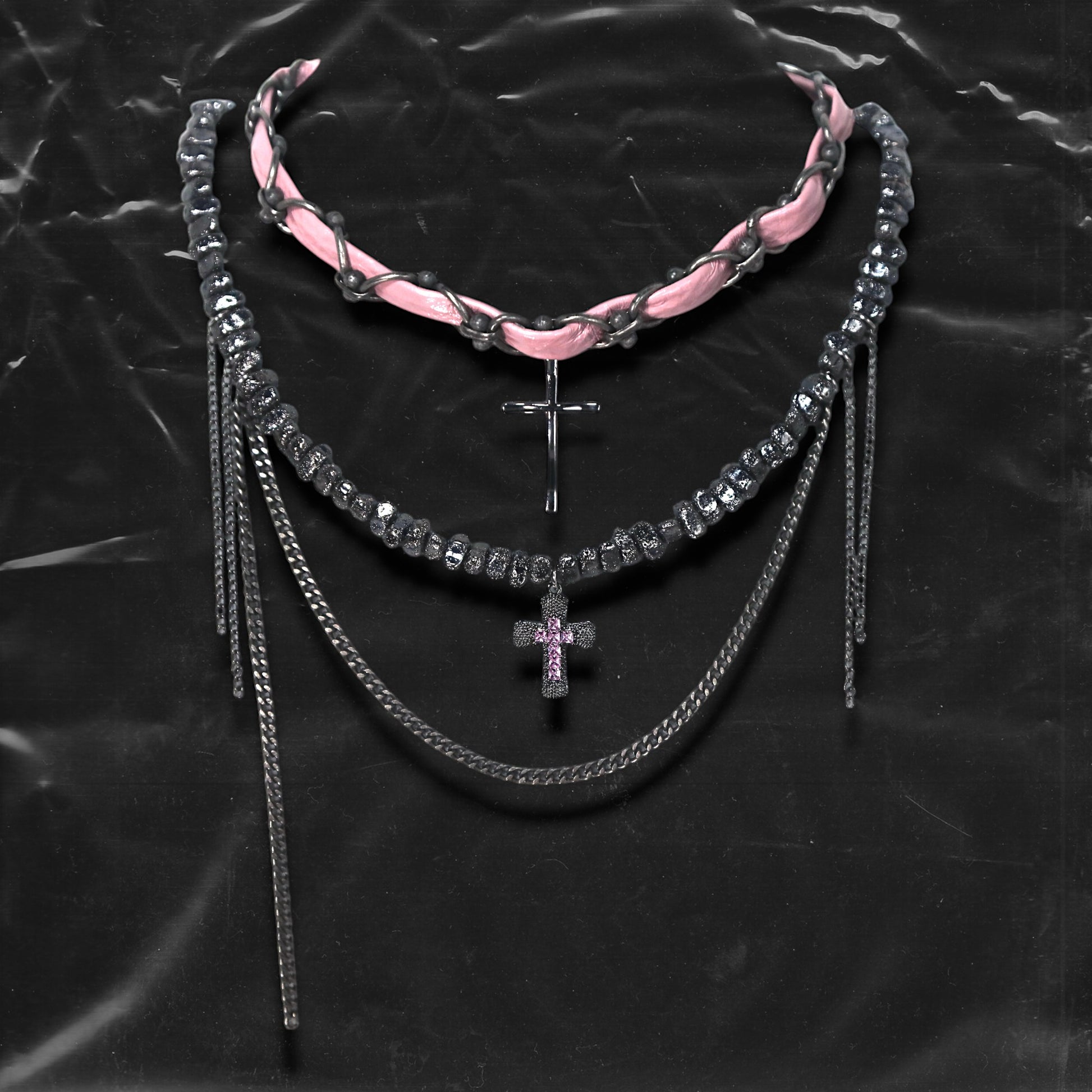 Chockychoker “Angel Trap” is a handcrafted dual-layer choker combining a braided pink faux leather strap interwoven with black-silver alloy components on the top layer, accented by a silver metal cross pendant. The lower layer features chunky metal beads with embossed, textured surfaces and a silver-tone cross charm embedded with light pink crystal-like stones. Multiple dangling silver chains add dimension and movement. This statement accessory making it ideal for Y2K, cyber-goth, punk,  and  rich materials