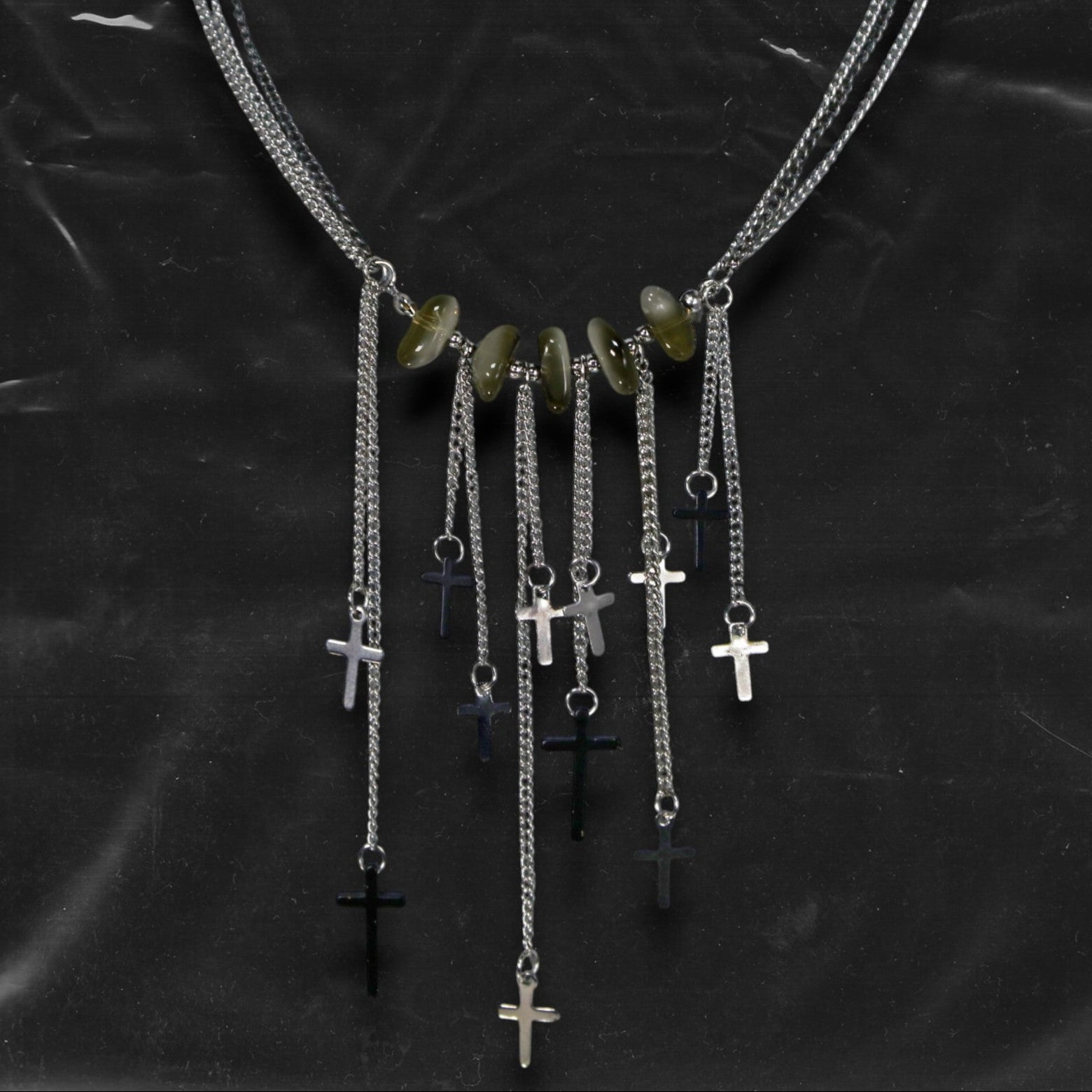 Chockychoker “Graviton Choir” Necklace is crafted from layered silver-toned fine chains, creating a fluid, multi-dimensional silhouette. The center is accented with amber glass beads, Along the lower edge, silver cross pendants are arranged in a staggered pattern. Blending gothic mystique and religious symbolism with Y2K futurism and industrial-punk edge, this piece is perfect for those drawn to dark romanticism, layered accessories, and strong visual presence in styling.
