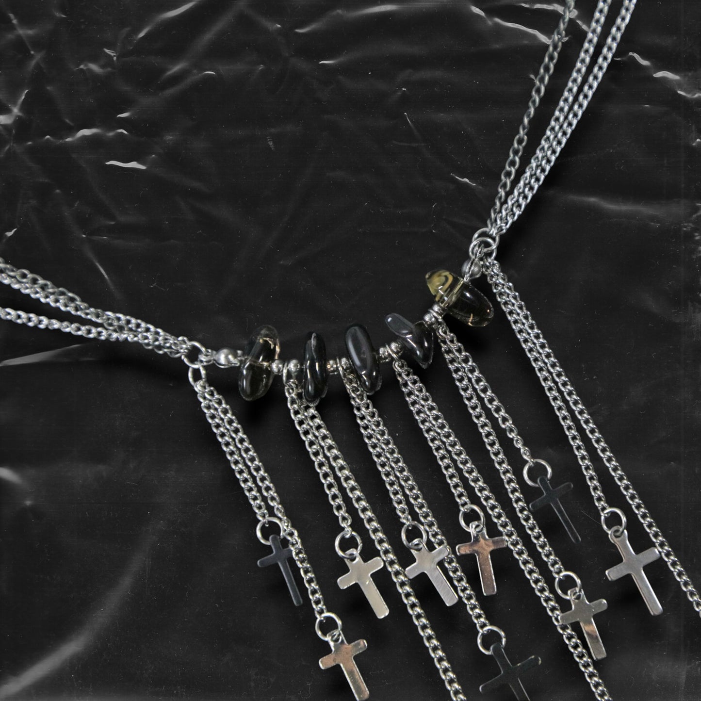 Chockychoker “Graviton Choir” Necklace is crafted from layered silver-toned fine chains, creating a fluid, multi-dimensional silhouette. The center is accented with amber glass beads, Along the lower edge, silver cross pendants are arranged in a staggered pattern. Blending gothic mystique and religious symbolism with Y2K futurism and industrial-punk edge, this piece is perfect for those drawn to dark romanticism, layered accessories, and strong visual presence in styling.
