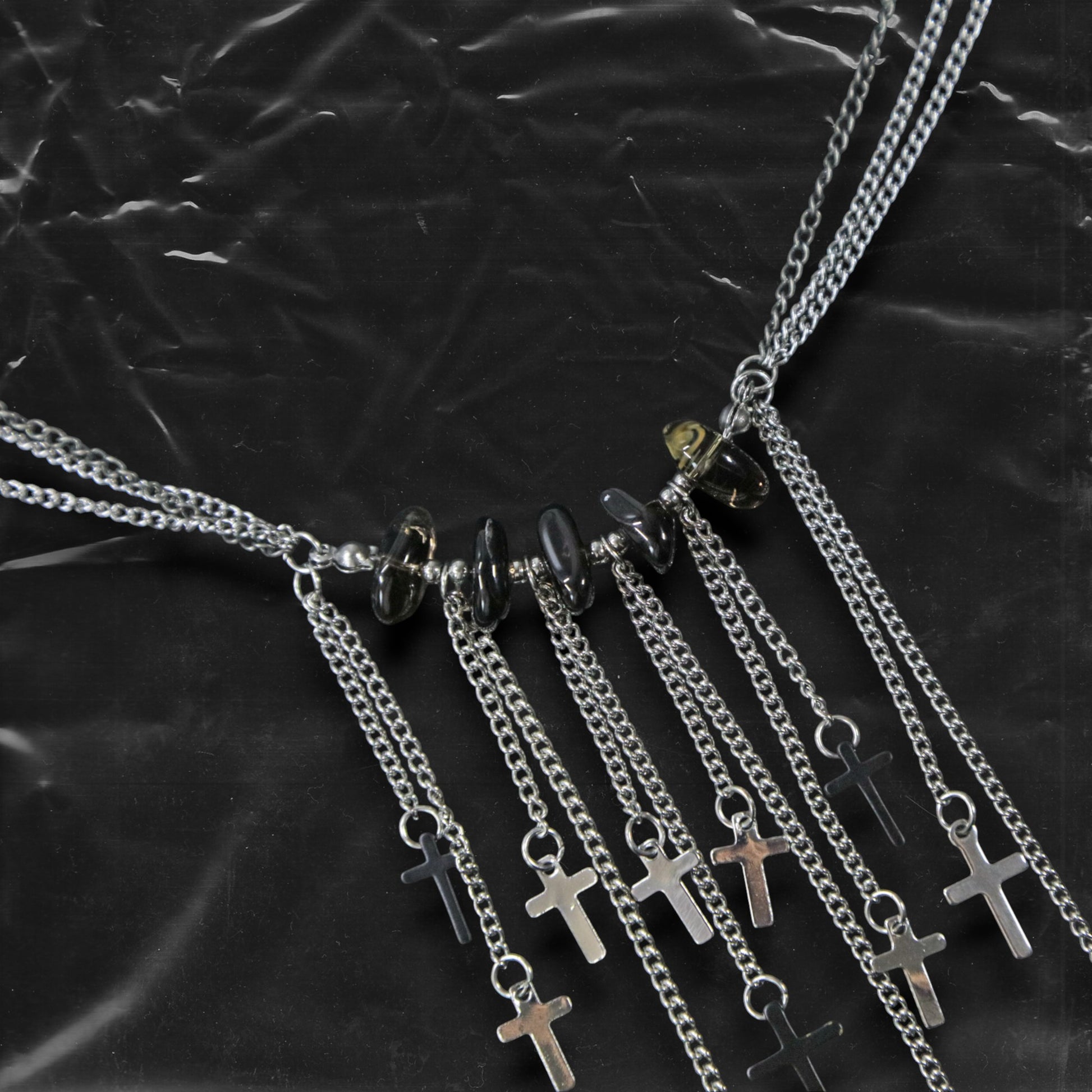 Chockychoker “Graviton Choir” Necklace is crafted from layered silver-toned fine chains, creating a fluid, multi-dimensional silhouette. The center is accented with amber glass beads, Along the lower edge, silver cross pendants are arranged in a staggered pattern. Blending gothic mystique and religious symbolism with Y2K futurism and industrial-punk edge, this piece is perfect for those drawn to dark romanticism, layered accessories, and strong visual presence in styling.
