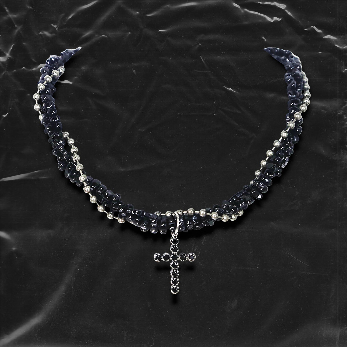 Chockychoker “Midnight Stitch” choker features a layered design made of black beads and silver-tone faux pearls, centered with a black rhinestone-studded cross pendant. The necklace blends gothic and Y2K influences with bold contrast and structured detail. A perfect statement piece for gothic, punk, alt, emo, and fashion-forward styles.