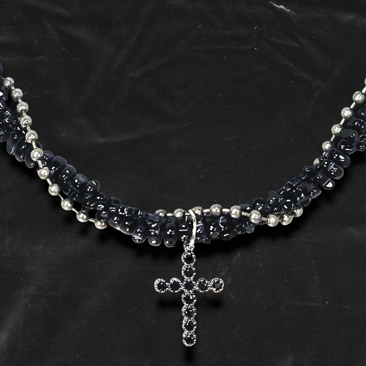 Chockychoker “Midnight Stitch” choker features a layered design made of black beads and silver-tone faux pearls, centered with a black rhinestone-studded cross pendant. The necklace blends gothic and Y2K influences with bold contrast and structured detail. A perfect statement piece for gothic, punk, alt, emo, and fashion-forward styles.