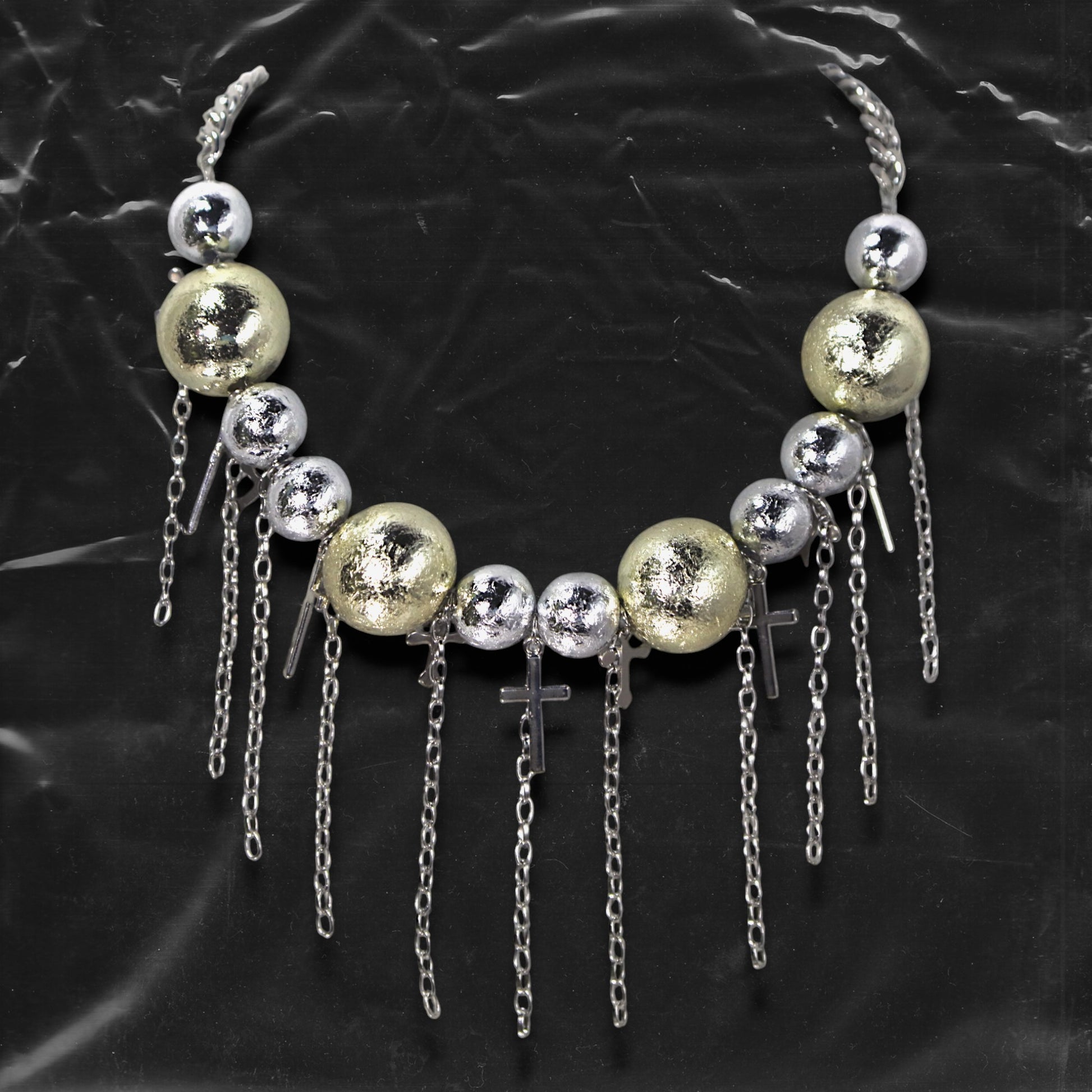 Chockychoker “ Mirror Pop ” is a Bold disco-inspired choker featuring large gold and silver reflective beads with a crackled-glass texture, silver-tone alloy cross pendants, and cascading metal chain tassels. This statement necklace merges glam and industrial aesthetics, ideal for lovers of disco, cyberpunk, rave, glam goth, and edgy Y2K fashion.
