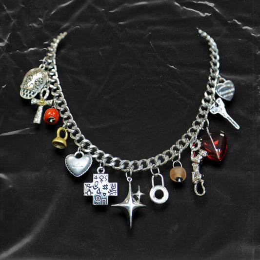 Chockychoker "Moonlit Relic" choker featuring a thick silver-tone chain adorned with eclectic dangling charms, including a crystal-eyed skull, metallic hearts, engraved cross, cosmic star, abstract rings, red gem heart, and vintage-style miniatures like a bell, shell, and keys. This mixed-media statement piece blends Y2K, gothic, alt, and symbolic aesthetics for bold and expressive styling.

