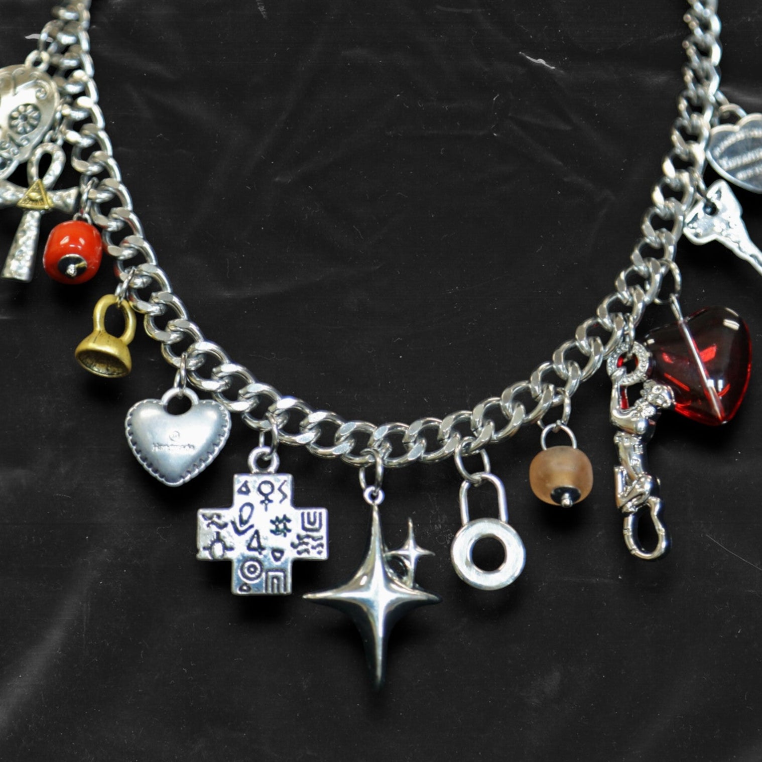 Chockychoker "Moonlit Relic" choker featuring a thick silver-tone chain adorned with eclectic dangling charms, including a crystal-eyed skull, metallic hearts, engraved cross, cosmic star, abstract rings, red gem heart, and vintage-style miniatures like a bell, shell, and keys. This mixed-media statement piece blends Y2K, gothic, alt, and symbolic aesthetics for bold and expressive styling.

