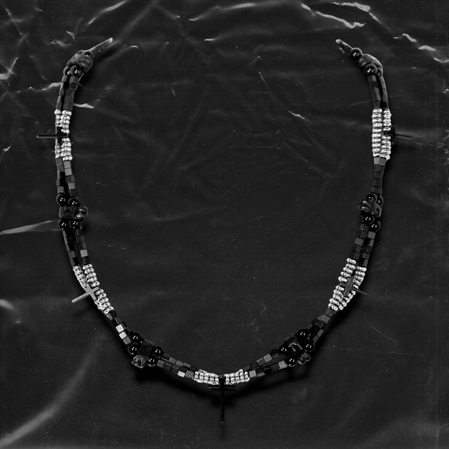 Chockychoker “Obsidian Code” is a meticulously constructed double layered necklace featuring interwoven black and silver gradient square beads, accented with metallic silver rounds and black beads for a cool, shadowy palette. Adorned with a series of small silver and black cross pendants, while black star-shaped charms add an extra layer of gothic detailing. Blending Y2K, darkwear, punk, and futuristic aesthetics, seeking edgy, gender-neutral accessories with strong streetwear appeal.