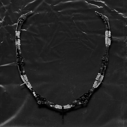 Chockychoker “Obsidian Code” is a meticulously constructed double layered necklace featuring interwoven black and silver gradient square beads, accented with metallic silver rounds and black beads for a cool, shadowy palette. Adorned with a series of small silver and black cross pendants, while black star-shaped charms add an extra layer of gothic detailing. Blending Y2K, darkwear, punk, and futuristic aesthetics, seeking edgy, gender-neutral accessories with strong streetwear appeal.