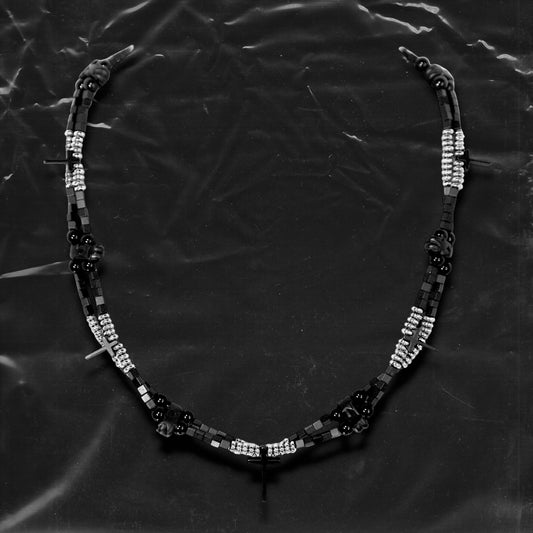 Chockychoker “Obsidian Code” is a meticulously constructed double layered necklace featuring interwoven black and silver gradient square beads, accented with metallic silver rounds and black beads for a cool, shadowy palette. Adorned with a series of small silver and black cross pendants, while black star-shaped charms add an extra layer of gothic detailing. Blending Y2K, darkwear, punk, and futuristic aesthetics, seeking edgy, gender-neutral accessories with strong streetwear appeal.