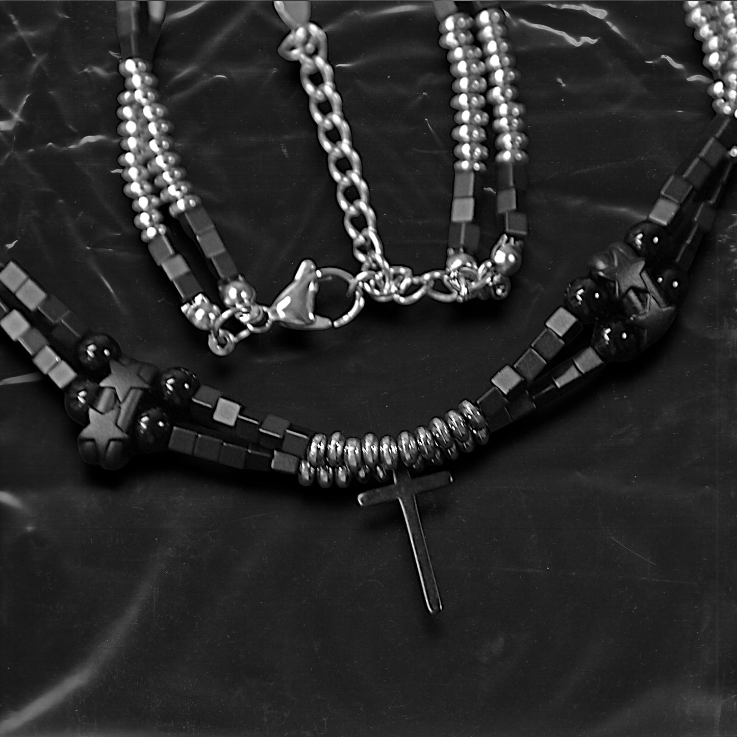 Chockychoker “Obsidian Code” is a meticulously constructed double layered necklace featuring interwoven black and silver gradient square beads, accented with metallic silver rounds and black beads for a cool, shadowy palette. Adorned with a series of small silver and black cross pendants, while black star-shaped charms add an extra layer of gothic detailing. Blending Y2K, darkwear, punk, and futuristic aesthetics, seeking edgy, gender-neutral accessories with strong streetwear appeal.