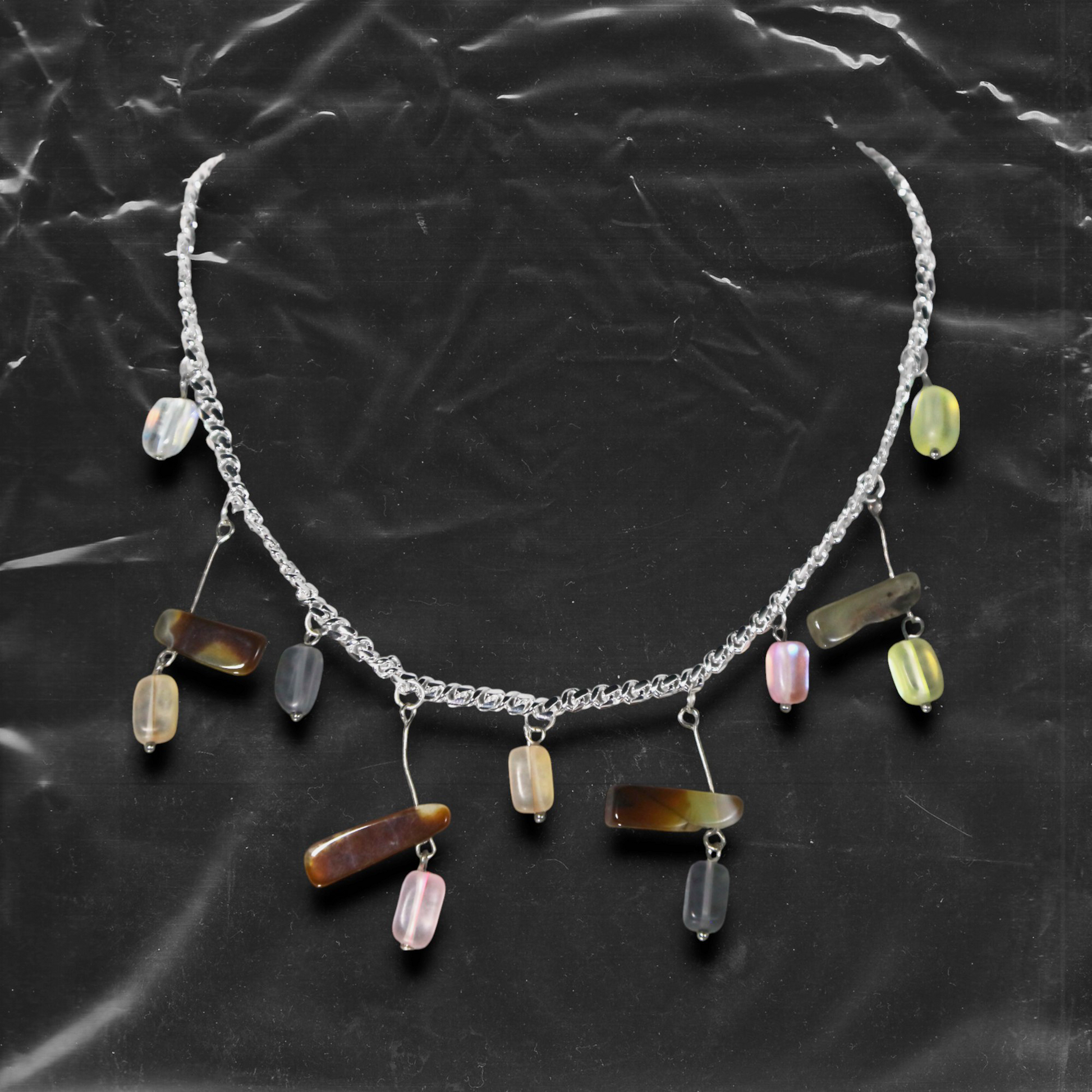 The Chockychoker "Stone Chime" choker features a delicate silver chain as its base, adorned with irregularly shaped colorful glass beads. These beads come in soft macaron tones lavender, mint green, buttery yellow, peachy pink, and amber brown with translucent , reminiscent of stones swaying in a breeze like wind chimes.The design draws inspiration from the playful color aesthetics of Y2K, the whimsical fairycore universe, and the imperfect charm of handcrafted jewelry