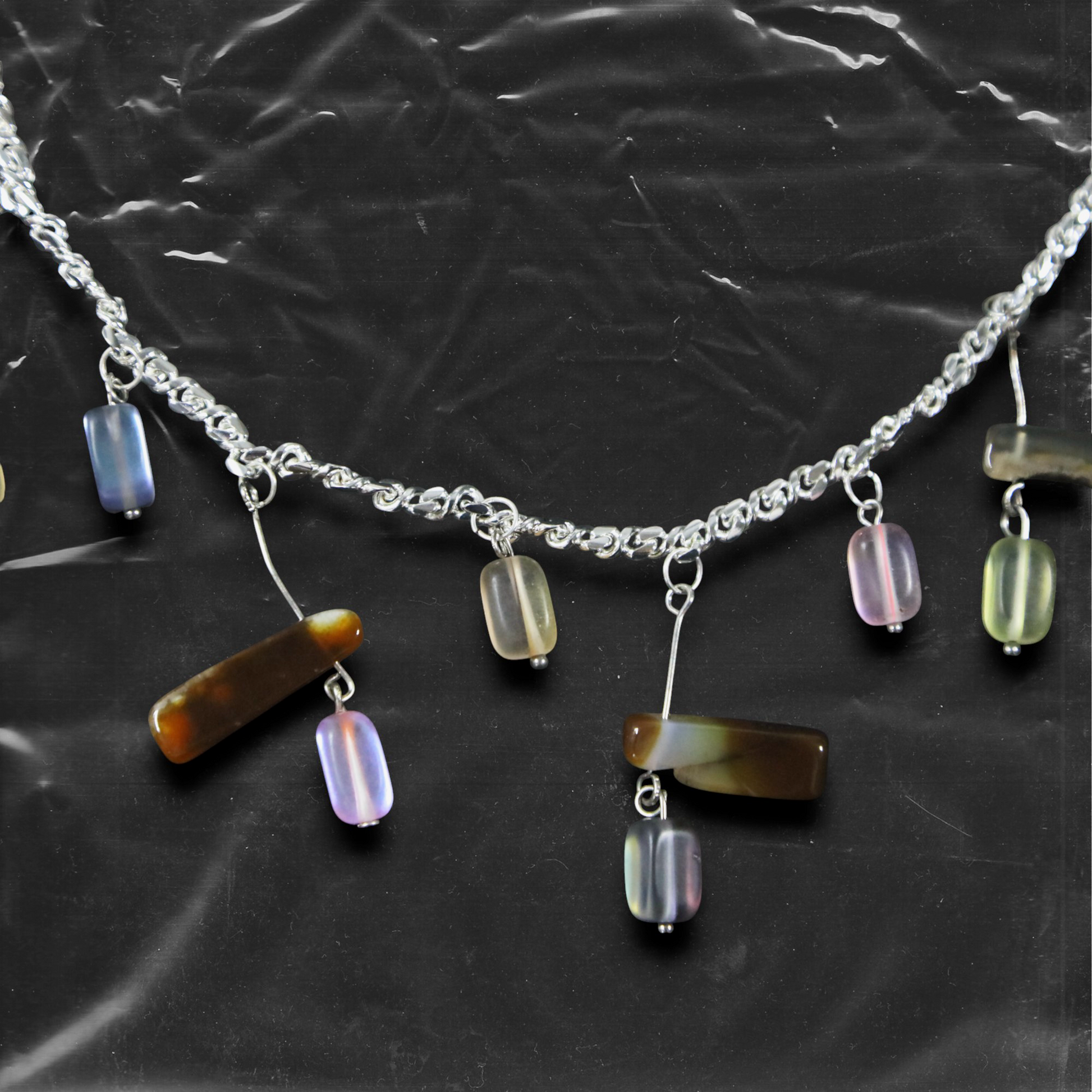 The Chockychoker "Stone Chime" choker features a delicate silver chain as its base, adorned with irregularly shaped colorful glass beads. These beads come in soft macaron tones lavender, mint green, buttery yellow, peachy pink, and amber brown with translucent , reminiscent of stones swaying in a breeze like wind chimes.The design draws inspiration from the playful color aesthetics of Y2K, the whimsical fairycore universe, and the imperfect charm of handcrafted jewelry
