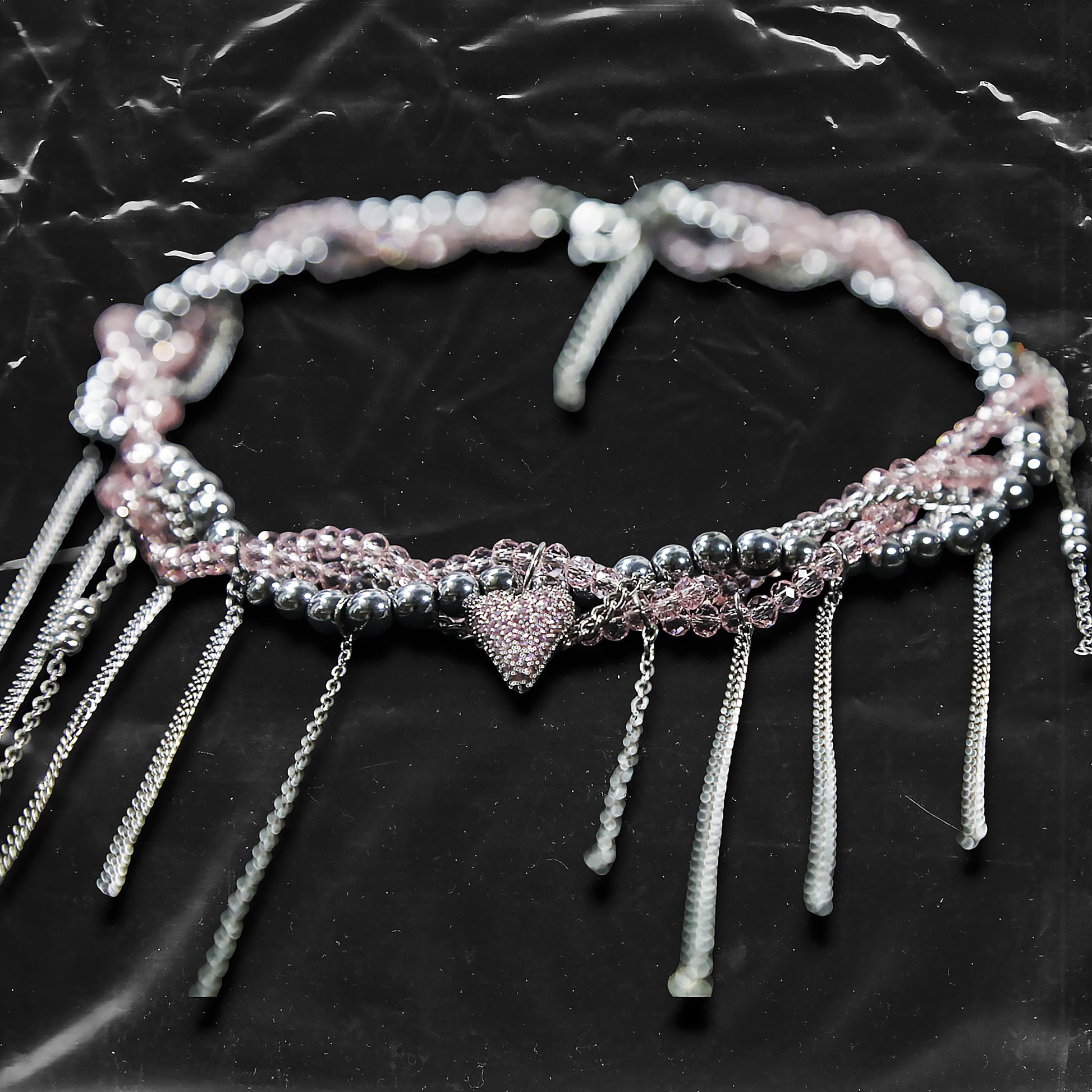Chockychoker “ Sugarglow ” is a Double-layer twisted choker combining pink knit yarn and metallic silver alloy beads, adorned with a central heart-shaped charm inlaid with pink crystals. The necklace features dangling silver chains, transparent pink crystal drops, and a single star charm, evoking both sweetcore and edgy glam aesthetics. Perfect for lovers of Y2K revival, coquette fashion, Harajuku streetwear, Materials include silver-tone alloy, faux crystals, acrylic yarn, and metal chains.