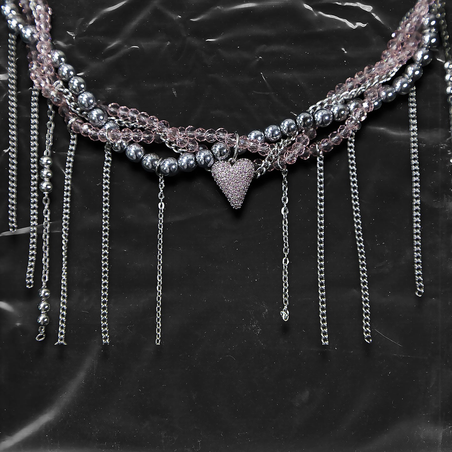 Chockychoker “ Sugarglow ” is a Double-layer twisted choker combining pink knit yarn and metallic silver alloy beads, adorned with a central heart-shaped charm inlaid with pink crystals. The necklace features dangling silver chains, transparent pink crystal drops, and a single star charm, evoking both sweetcore and edgy glam aesthetics. Perfect for lovers of Y2K revival, coquette fashion, Harajuku streetwear, Materials include silver-tone alloy, faux crystals, acrylic yarn, and metal chains.