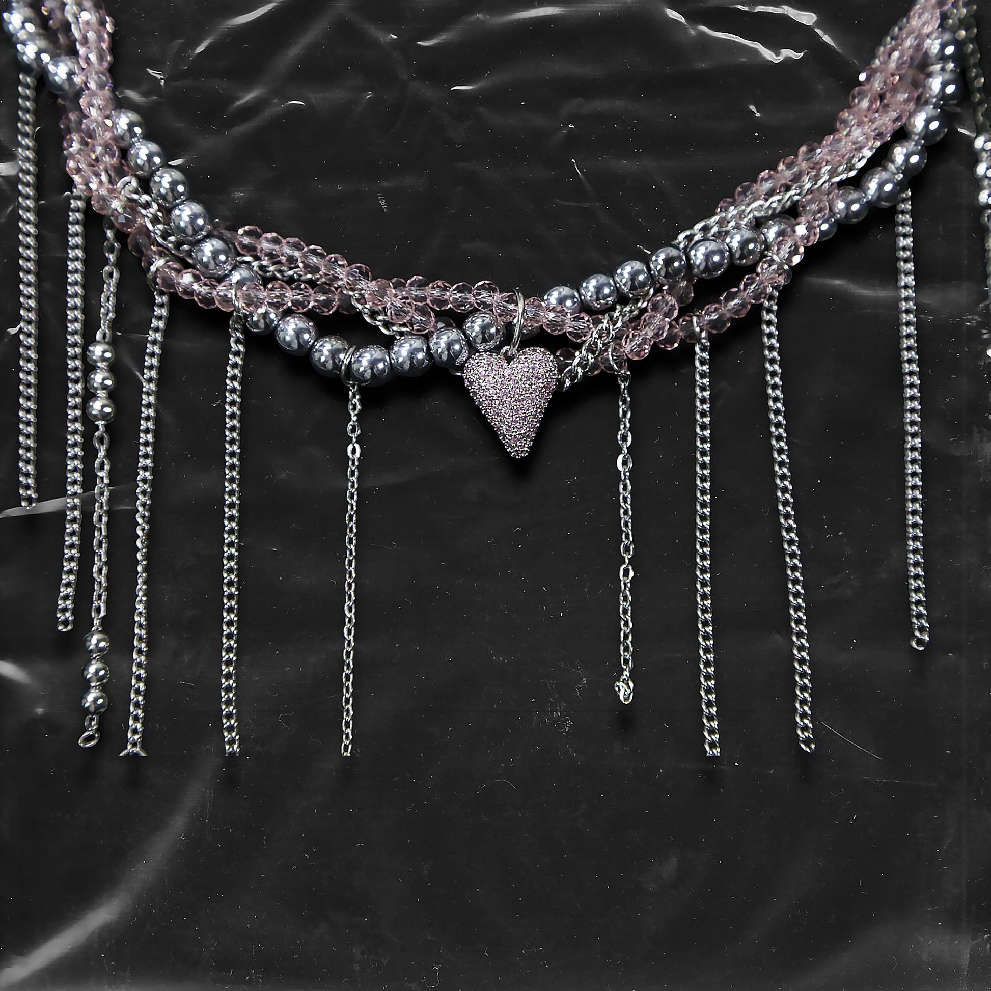 Chockychoker “ Sugarglow ” is a Double-layer twisted choker combining pink knit yarn and metallic silver alloy beads, adorned with a central heart-shaped charm inlaid with pink crystals. The necklace features dangling silver chains, transparent pink crystal drops, and a single star charm, evoking both sweetcore and edgy glam aesthetics. Perfect for lovers of Y2K revival, coquette fashion, Harajuku streetwear, Materials include silver-tone alloy, faux crystals, acrylic yarn, and metal chains.