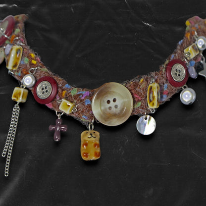 Chockychoker “Teddy Patch I” is a handcrafted choker made from colorful handwoven  yarn, featuring a central oversized iridescent brown button, ceramic bear chapendant, shell accents, pearl-like beads, translucent resin blocks, layered silver-tone chains, metallic star charm, glossy red and mixed buttons, and scattered gemstone-style plastic beads. Rich in textures and asymmetrical charm arrangement eclectic necklace embodies . Ideal for Y2K, gothic, indie, Harajuku, grunge, artsy, retro, alt,  boho fashion