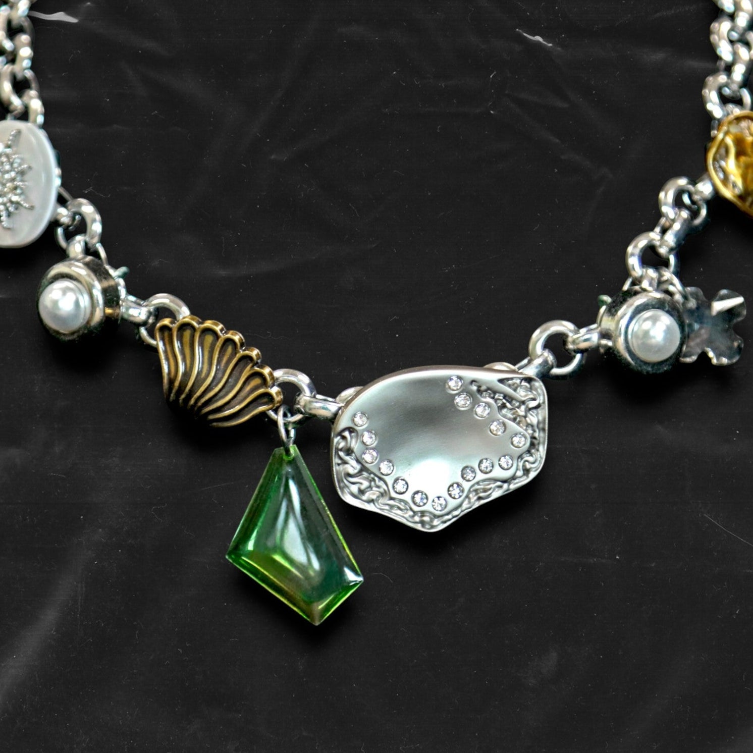 Chockychoker "Witch's Pocket" choker features a whimsical mix of charms, including sculpted silver-toned metal, a delicate milky-white button set with a snowflake-shaped faux crystal, a gold shell charm, faux pearls, a translucent green gemstone pendant, engraved medallions, and abstract vintage elements. The overall style blends eccentricity, fairycore, vintage, witchy, and Y2K aesthetics—perfect for those who embrace unique and expressive fashion.