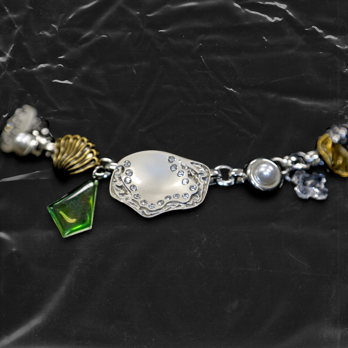 Chockychoker "Witch's Pocket" choker features a whimsical mix of charms, including sculpted silver-toned metal, a delicate milky-white button set with a snowflake-shaped faux crystal, a gold shell charm, faux pearls, a translucent green gemstone pendant, engraved medallions, and abstract vintage elements. The overall style blends eccentricity, fairycore, vintage, witchy, and Y2K aesthetics—perfect for those who embrace unique and expressive fashion.