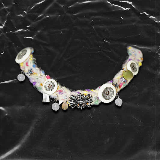 Chockychoker “Woolen Wish” is a handmade choker crafted from multicolored yarn with green, purple, yellow, and pink. Adorned with white and metallic vintage-style buttons, iridescent translucent beads, opalescent shell discs, and an ornate silver-tone floral centerpiece. Accents include soft textured fibers, dangling orb charms, and layered mixed materials that add depth and movement. A harmonious mix of fairycore, cottagecore, Y2K, and alternative aesthetic perfect for indie, vintage inspired, boho, artis
