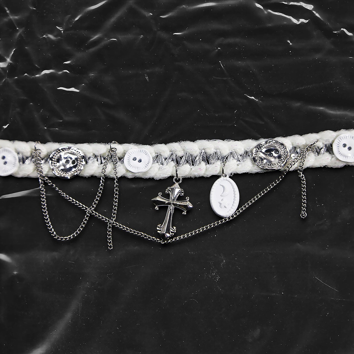 Chockychoker “Milk Galaxy” is a Handcrafted gothic-style choker made from soft white yarn interwoven with shimmering silver thread, adorned with layered silver-tone chains, a central baroque-style silver cross pendant, a mix of glossy white plastic buttons and vintage-style metallic buttons, and white oval resin charms ideal for lovers of gothic, alt, punk, lolita, soft grunge, and romantic street fashion. Perfect for those seeking statement chokers with unique handcrafted details and mixed media textures.