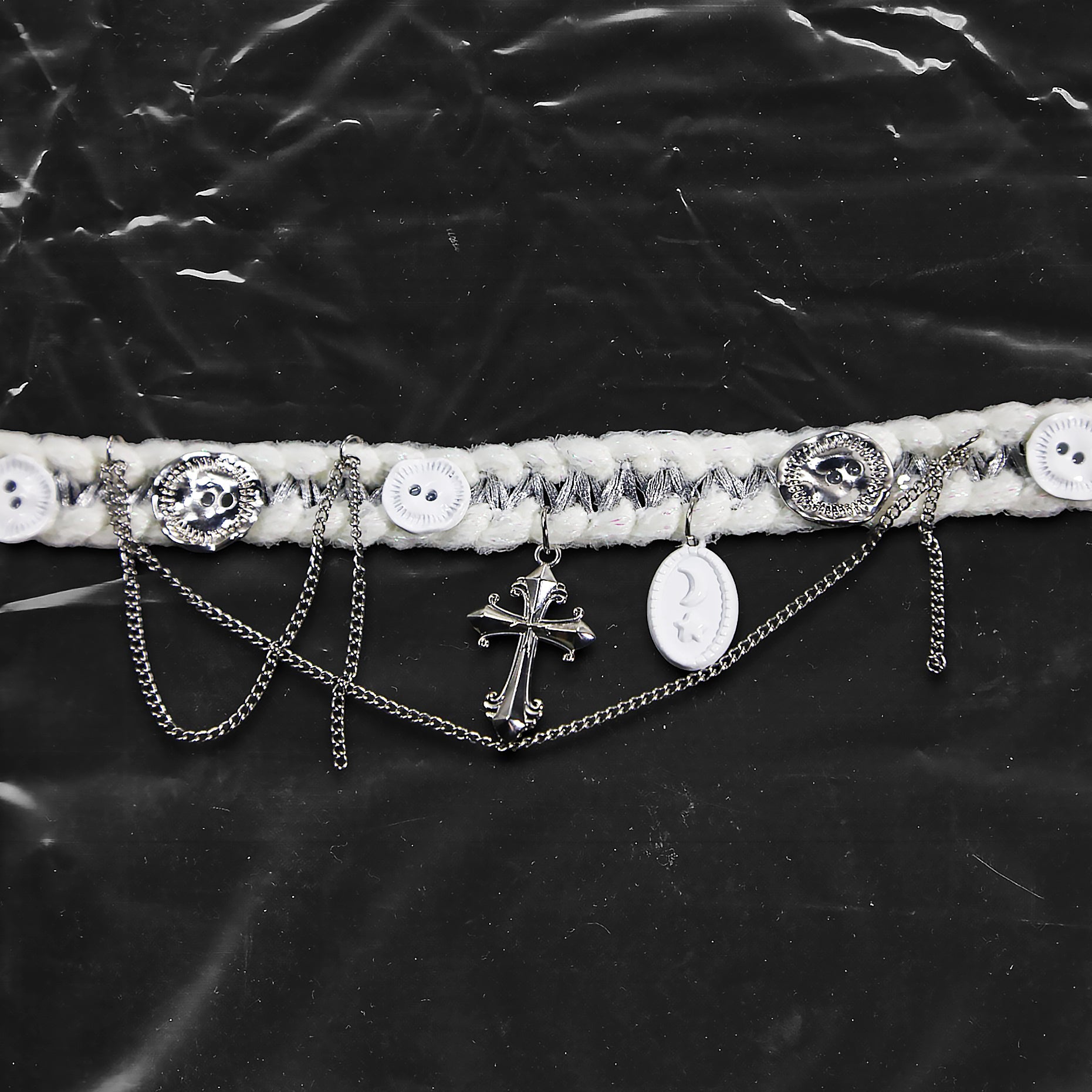 Chockychoker “Milk Galaxy” is a Handcrafted gothic-style choker made from soft white yarn interwoven with shimmering silver thread, adorned with layered silver-tone chains, a central baroque-style silver cross pendant, a mix of glossy white plastic buttons and vintage-style metallic buttons, and white oval resin charms ideal for lovers of gothic, alt, punk, lolita, soft grunge, and romantic street fashion. Perfect for those seeking statement chokers with unique handcrafted details and mixed media textures.