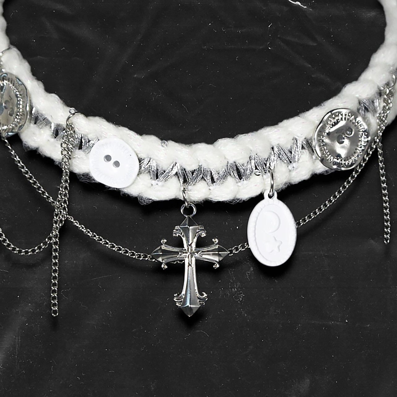 Chockychoker “Milk Galaxy” is a Handcrafted gothic-style choker made from soft white yarn interwoven with shimmering silver thread, adorned with layered silver-tone chains, a central baroque-style silver cross pendant, a mix of glossy white plastic buttons and vintage-style metallic buttons, and white oval resin charms ideal for lovers of gothic, alt, punk, lolita, soft grunge, and romantic street fashion. Perfect for those seeking statement chokers with unique handcrafted details and mixed media textures.