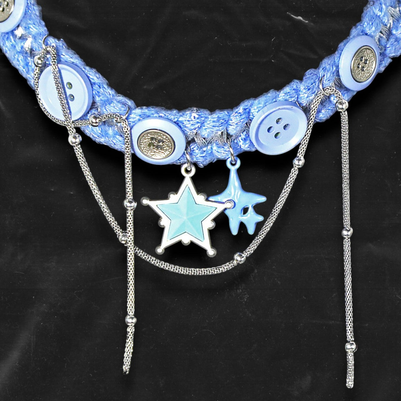 Chockychoker "Blue Save Point"  handmade choker featuring  blue star pendants in resin   finish, accented with silver-tone chains of mixed texture, and secured onto a woven light blue yarn base. Decorated with multiple blue and silver-tone buttons along the band. This piece combines  star motifs , creating a unique blend of sweet-cool , alt, Harajuku, cyberpop, and soft punk aesthetics.  Materials include yarn, alloy buttons, silver-tone metal chains, and enamel resin charms.
