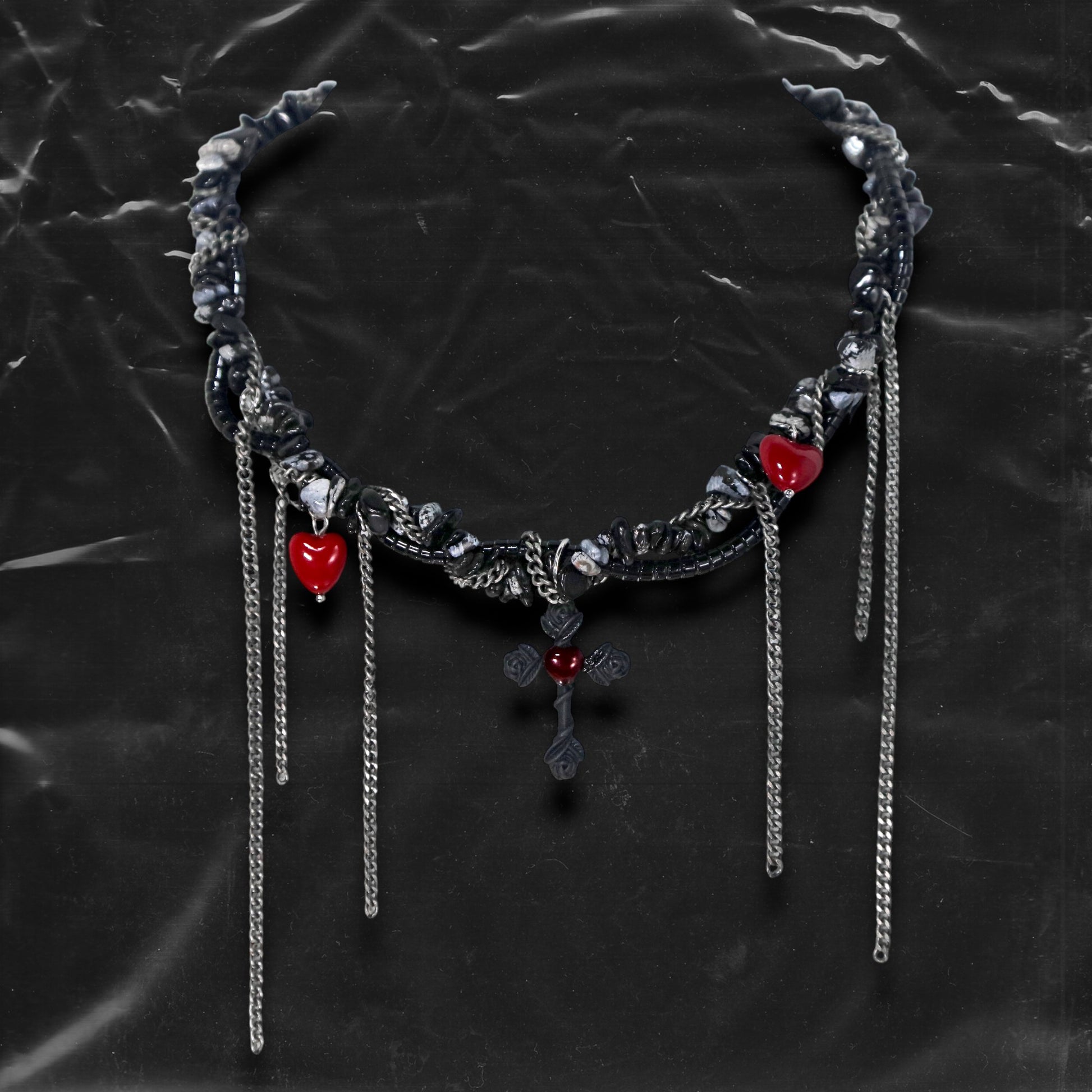 Chockychoker “Oath Object” is a gothic-inspired black ribbon choker featuring textured silver embellishments, dramatic silver-tone chain fringe, deep red heart charms, and a matte black cross pendant with floral details. Combining dark romance with edgy elements, this handcrafted piece blends punk, goth, emo, and Y2K aesthetics—perfect for those who love statement jewelry with emotional and symbolic undertones.
