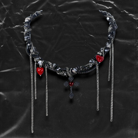 Chockychoker “Oath Object” is a gothic-inspired black ribbon choker featuring textured silver embellishments, dramatic silver-tone chain fringe, deep red heart charms, and a matte black cross pendant with floral details. Combining dark romance with edgy elements, this handcrafted piece blends punk, goth, emo, and Y2K aesthetics—perfect for those who love statement jewelry with emotional and symbolic undertones.
