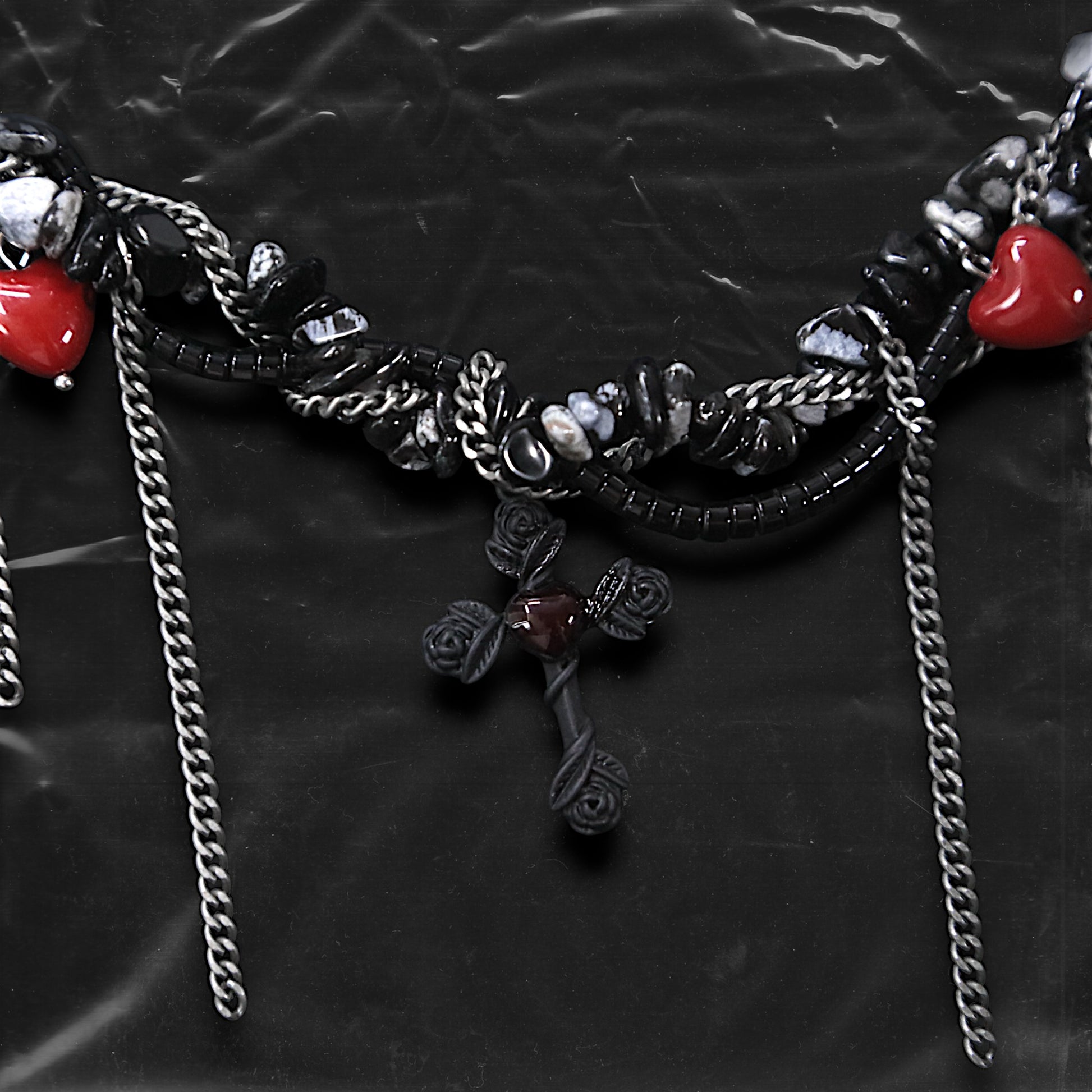 Chockychoker “Oath Object” is a gothic-inspired black ribbon choker featuring textured silver embellishments, dramatic silver-tone chain fringe, deep red heart charms, and a matte black cross pendant with floral details. Combining dark romance with edgy elements, this handcrafted piece blends punk, goth, emo, and Y2K aesthetics—perfect for those who love statement jewelry with emotional and symbolic undertones.

