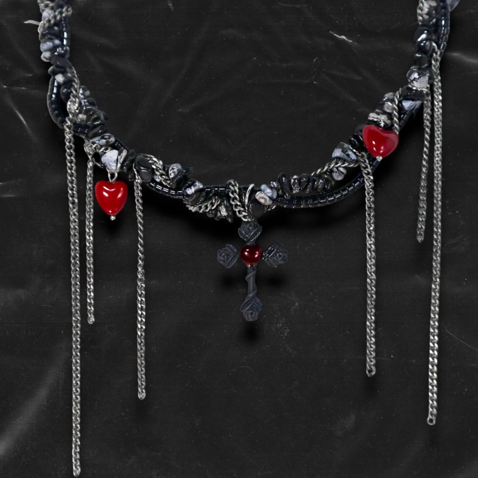 Chockychoker “Oath Object” is a gothic-inspired black ribbon choker featuring textured silver embellishments, dramatic silver-tone chain fringe, deep red heart charms, and a matte black cross pendant with floral details. Combining dark romance with edgy elements, this handcrafted piece blends punk, goth, emo, and Y2K aesthetics—perfect for those who love statement jewelry with emotional and symbolic undertones.
